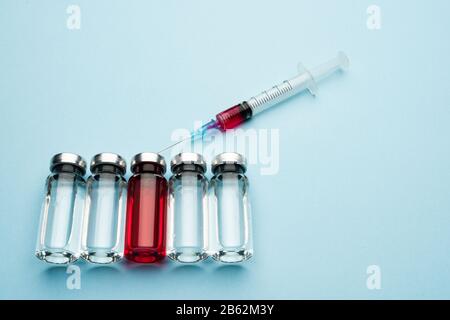 Una fila di flaconcini per uso medico. Bottiglie di vetro con un medicinale trasparente e una con rosso Foto Stock