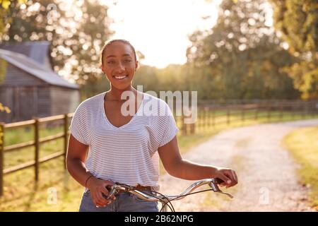 Ritratto Di Giovane Donna Equitazione In Bicicletta Lungo Country Lane Al Tramonto Foto Stock