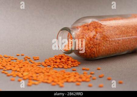 lenticchie rosse divise sparse su uno sfondo grigio da vaso di vetro Foto Stock