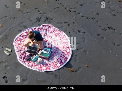 Uno studente con il suo portatile n libri di studio sulla spiaggia Foto Stock