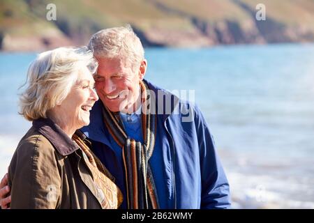 Amorevole Coppia Senior Abbracciando Come Camminare Lungo Shoreline Di Spiaggia Da Onde Foto Stock