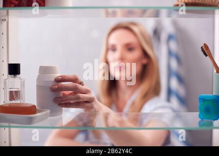 Vista Attraverso Bagno Gabinetto Di Giovane Donna Che Prende Il Farmaco Dal Contenitore Foto Stock