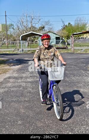 Donna anziana, indossando un casco di sicurezza, imparando a cavalcare la sua bicicletta donata appena acquisita. Foto Stock