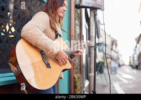 Femmina Musicista Busking In Riproduzione Chitarra Acustica All'Aperto In Strada Foto Stock