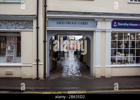 Un arco tra 2 negozi con il titolo 'Old Swan Yard' sopra di esso, con un sentiero flagstone per piccoli negozi nella città Wiltshire di Devizes Foto Stock