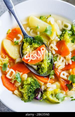 Zuppa di alfabeto sana per bambini con verdure e noodle in piatti bianchi. Concetto di cibo per bambini.