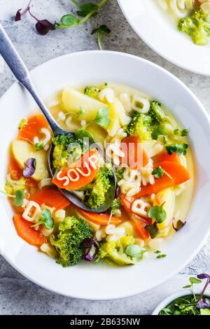 Zuppa di alfabeto sana per bambini con verdure e noodle in piatti bianchi. Concetto di cibo per bambini.