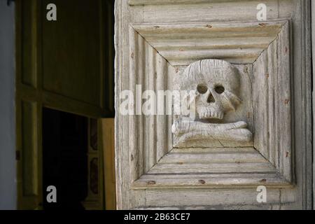 Primo piano della porta medievale in legno con teschio e ossa scolpite all'ingresso della Chiesa del Purgatorio di Matera. Foto Stock