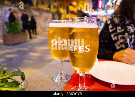 Due birre turche locali su un tavolo come una donna scrive le note ad un tavolo di un caffè all'aperto in un'area colorfully illuminata di Istanbul, Turchia, di notte. Foto Stock