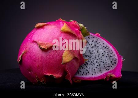 Primo piano di due metà di una Pitaya o Dragon Fruit a polpa bianca con guscio esterno e polpa bianca con semi neri su una superficie nera Foto Stock