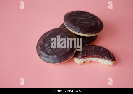 Un mucchio di torte Jaffa. Biscotto di amaro coperto di cioccolato fondente e riempito con fragola rosa o marmellata di ciliegie. Deliziosi biscotti isolati su sfondo rosa con copyspace Foto Stock