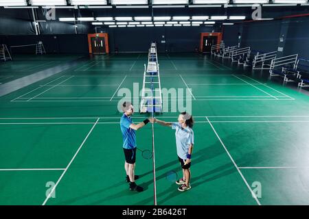 Giovani giocatori di badminton maschio e femmina scuotono le mani dopo l'allenamento in palestra Foto Stock