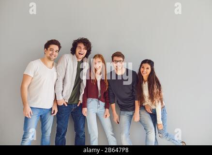 Gruppo di giovani in abiti casual sorridenti mentre sfondo grigio. Foto Stock