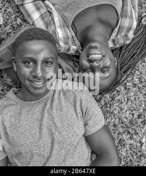 Felice sorridente adolescenti. Coppia afroamericana che si posa in erba, volti di donna e uomo accanto a vicenda guardando verso l'alto la macchina fotografica. Foto Stock