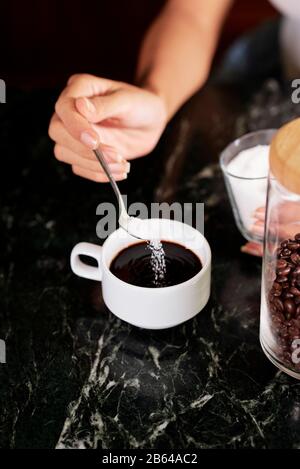 Immagine ravvicinata della donna che mette un cucchiaio di zucchero in una tazza di caffè Foto Stock