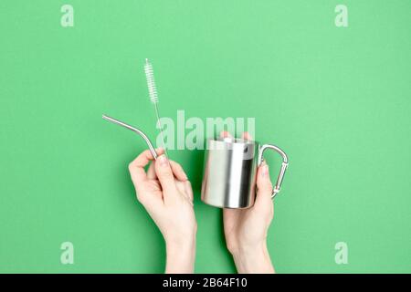 Il tubo metallico, la tazza e la spazzola per la pulizia sono in posizione di presa per le mani. Concetto di zero sprechi su sfondo verde. Foto Stock