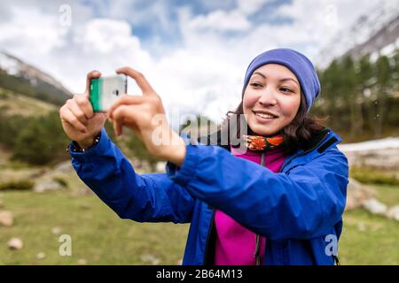 Giovane donna escursionista scattare foto con smartphone su montagna picco in primavera Foto Stock