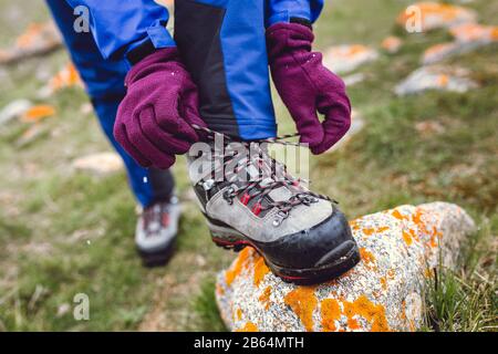 Hiker che stringe i lacci dello scarpone sulla roccia, in alto in montagna Foto Stock