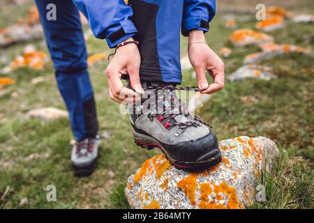 Hiker che stringe i lacci dello scarpone sulla roccia, in alto in montagna Foto Stock