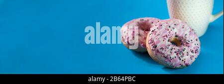 Ciambelle smaltate con una tazza di caffè su sfondo blu. Foto Stock