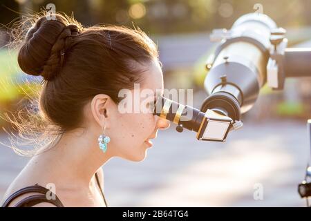 Giovane donna sorridente che guarda verso il cielo attraverso il telescopio astronomico Foto Stock