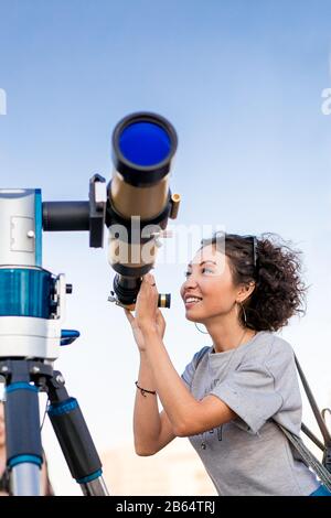 Giovane donna sorridente che guarda verso il cielo attraverso il telescopio astronomico Foto Stock