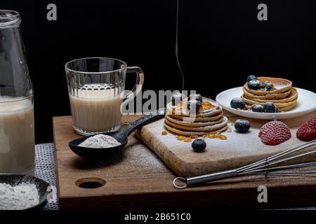 Pila di frittelle fatte in casa con fragole di frutta fresca e mirtilli su un tavolo di legno con zucchero uno sciroppo di miele, vanila mano di bellezza dolce Foto Stock