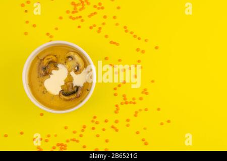 Zuppa di piselli con funghi in una piastra rosa si erge su uno sfondo giallo, intorno alla dispersione di semi di lenticchie Foto Stock