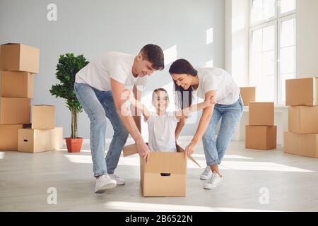 Una famiglia felice sta divertendosi giocando con una scatola sul pavimento in un nuovo appartamento. Foto Stock