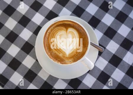 Caffè bianco piatto perfetto con rotazione del cuore su un panno bianco e nero da tavolo Foto Stock