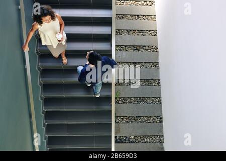 Gli uomini d'affari che si trovano su gradini nell'edificio moderno degli uffici e che discutono le ultime notizie, vista dall'alto Foto Stock