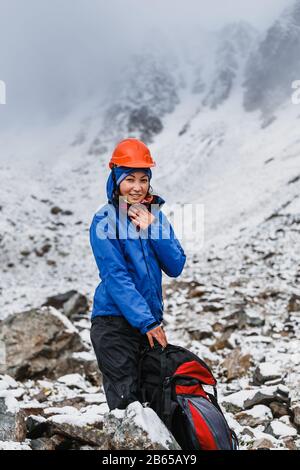 Donna In Casco con zaino su Snow Covered Mountain Top Godere di vista. Foto Stock