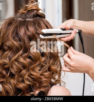 Parrucchiere usando un ferro arricciacapelli o tenaglie per impresa boccoli  di capelli lunghi marrone di un client femmina Foto stock - Alamy