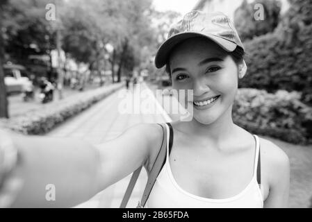 Felice giovane bella ragazza turistica asiatica prendere selfie nelle strade della città Foto Stock