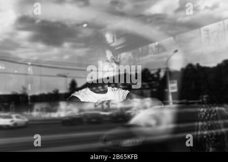 Attraente giovane donna seduto al tavolo in caffetteria. Fotografato dalla strada con riflessi della città nella finestra Foto Stock