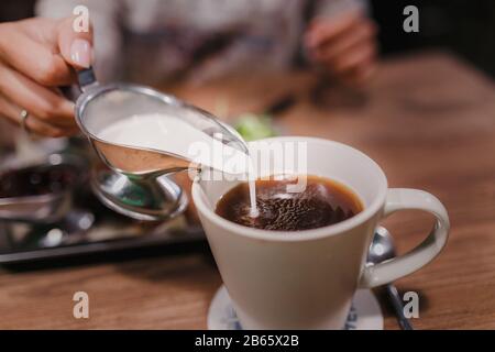 Mungendo che è versato in tazza di caffè. Filtro e grana aggiunti per effetto pellicola Foto Stock