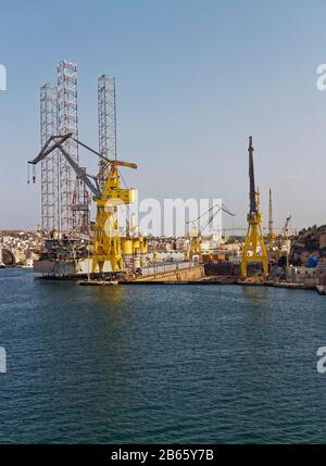 Un Dry Dock Vuoto con le sue strutture portuali e gru associate, con un Oil Rig legato accanto ad esso nell'area occupata del Porto di Valletta. Foto Stock