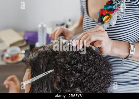 Primo piano di un parrucchiere che arriccia capelli neri corti con ferri da stiro. Foto Stock