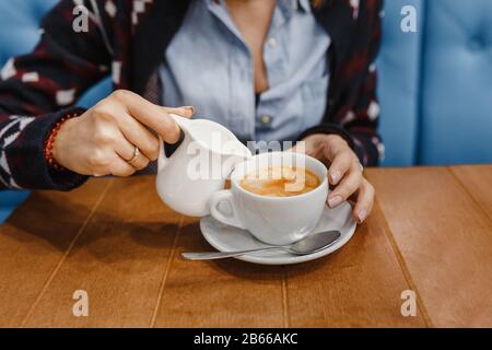 Donna che versa latte in tazza di tè dal bollitore Foto Stock