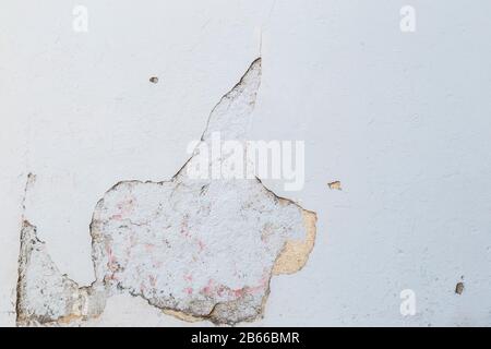 perde-su di un muro di calcestruzzo stagionato e vecchio, intonacatura dipinta in bianco è rotto. Sfondo a trama intera astratto ad alta risoluzione. Foto Stock