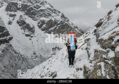 Scalatore a piedi su un ripido pendio innevato in montagna sullo sfondo di una scogliera e l'abisso. Il concetto di rischio e avventura all'aperto Foto Stock