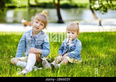 Adorabili bambini in jaket blu denim alla moda che si posa all'aperto. Ragazze che si divertono insieme. Bambine nel parco. Vacanze estive o primaverili Foto Stock