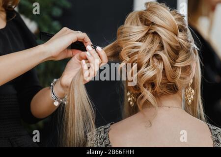 Il parrucchiere rende il bun superiore di nozze acconciatura primo piano su capelli sabbiosi biondi di bella donna Foto Stock