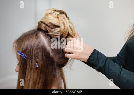 Il parrucchiere fa un hairstyle superiore del bun vicino-in su sui capelli marroni della donna bella Foto Stock