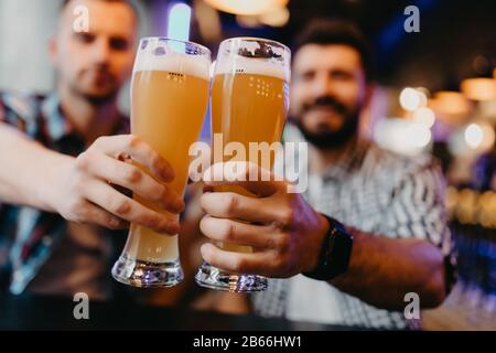 Amici felici che si abbacchiano con le tazze di birra nel pub, sorridendo. Foto Stock