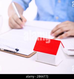 Concetto di affari - l'uomo asiatico giovane in camicia blu calcola, firma contratto per comprare un pagamento di prestito della casa, pagando l'assicurazione, l'imposta, primo piano. Foto Stock