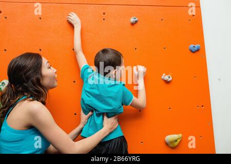 Madre che aiuta il suo ragazzo a salire su un muro in palestra bouldering sul parco giochi Foto Stock