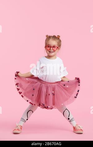 Infanzia felice. Ragazza bambino divertente in gonna tulle saltando e divertirsi isolato su sfondo rosa. Festeggiamo un carnevale vivace per i bambini, compleanno Foto Stock