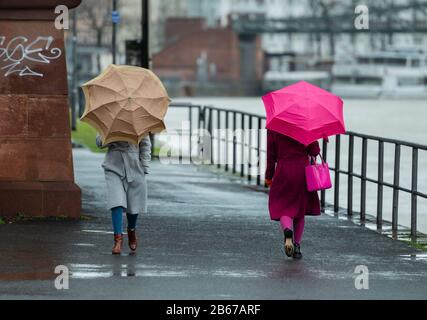 10 marzo 2020, Hessen, Francoforte sul meno: Due donne camminano lungo la riva principale del fiume con ombrelloni. Sullo sfondo si può vedere il ponte di ferro. Foto: Andreas Arnold/Dpa Foto Stock