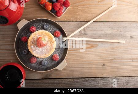 Torte giapponesi fatte in casa su uno sfondo di legno con lamponi, more e fragole e zucchero in polvere. Vista dall'alto. Foto Stock